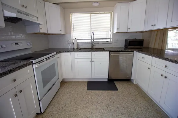 a kitchen with granite countertop white cabinets stainless steel appliances a sink and a window