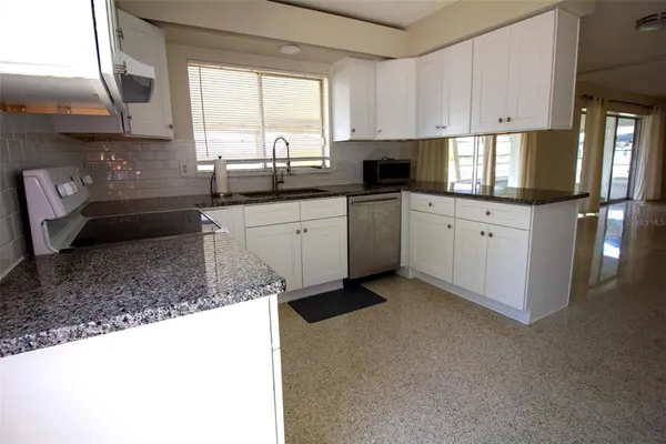 a kitchen with granite countertop a sink stainless steel appliances white cabinets and a window