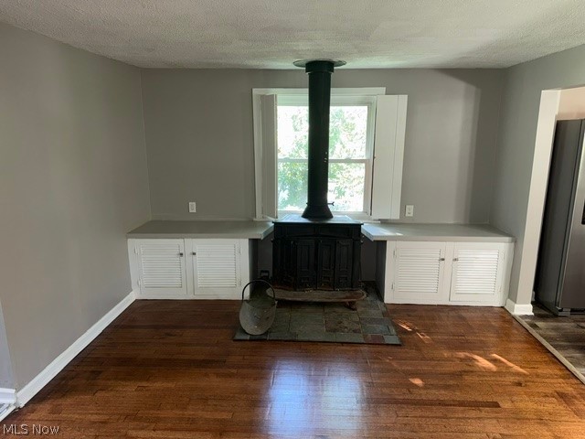 Hardwood flooring throughout, built-in cabinetry with white louvered doors, a wood-burning stove with a stone hearth, and a large window providing natural illumination