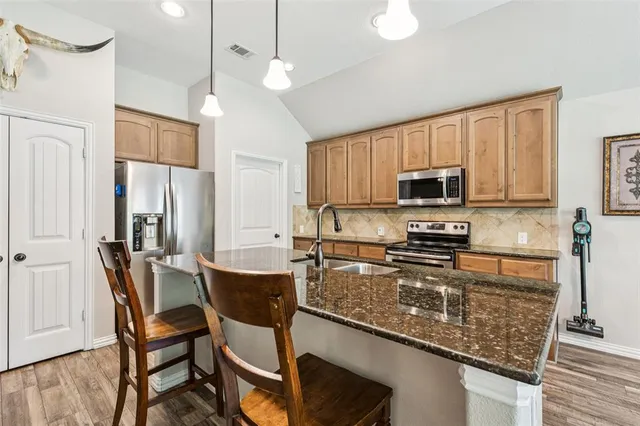 a kitchen with stainless steel appliances granite countertop a stove top oven a sink a dining table and chairs with wooden floor