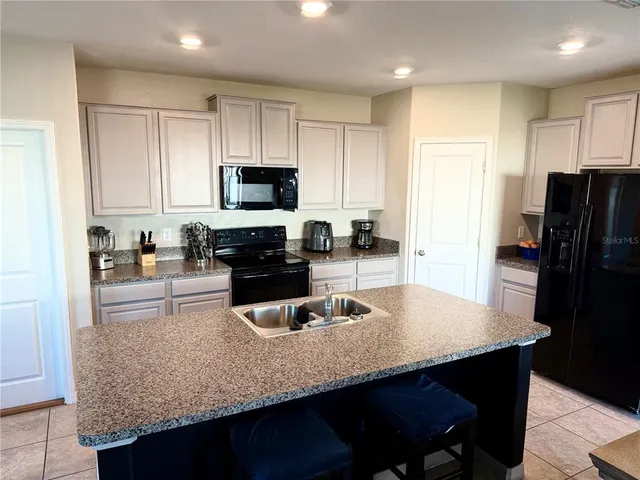 a kitchen with granite countertop a refrigerator a sink a stove a dining table and chairs