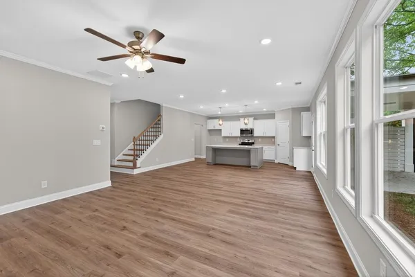 a view of an empty room with wooden floor a ceiling fan and windows