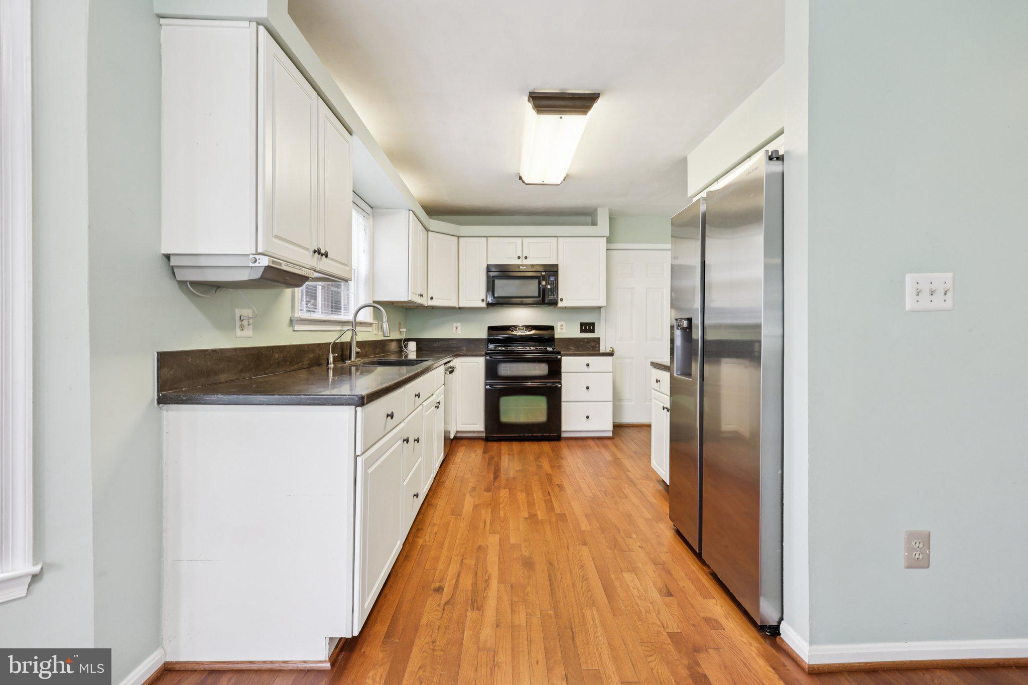 10457 Pineview Road Manassas, VA 20111 - Photo 7 of 55 a kitchen with granite countertop a refrigerator a sink dishwasher and white cabinets with wooden floor