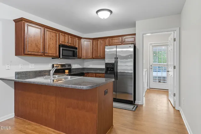 a large kitchen with stainless steel appliances granite countertop a stove a refrigerator a sink a microwave and island with wooden floor