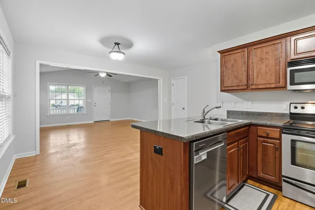 a kitchen with stainless steel appliances granite countertop a refrigerator a stove a sink and a microwave with wooden floor