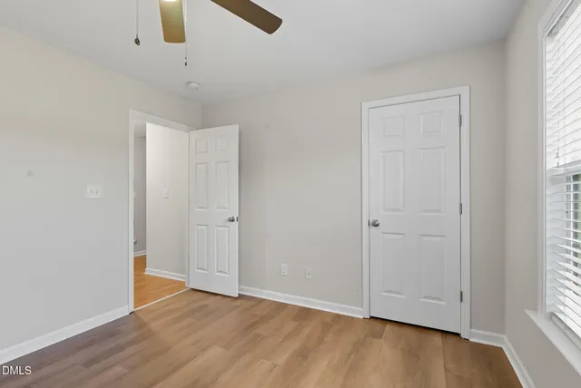an empty room with wooden floor windows and fan