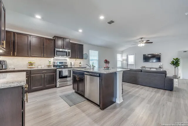 a kitchen with stainless steel appliances kitchen island granite countertop a stove a sink dishwasher a refrigerator and a oven with wooden floor