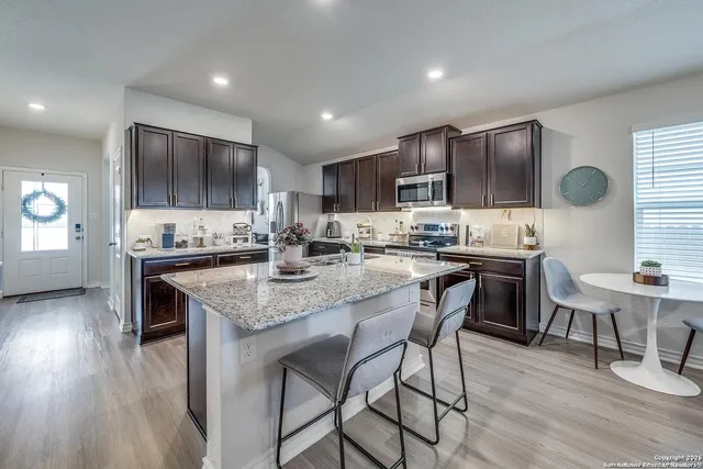 a kitchen with kitchen island granite countertop wooden floors cabinets a dining table and appliances