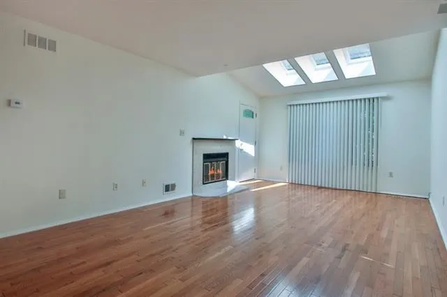 a view of an empty room with wooden floor fireplace and a window