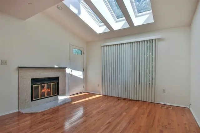 a view of an empty room with wooden floor fireplace and a window