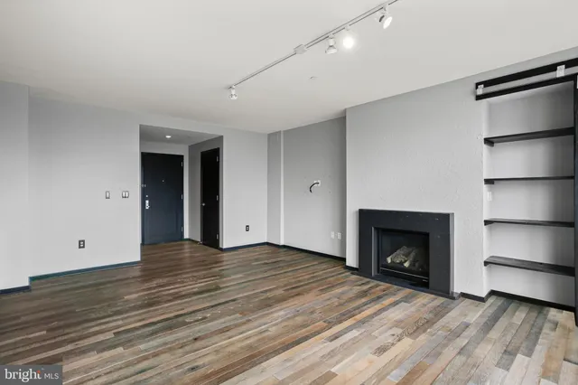 a view of an empty room with wooden floor fireplace and a window