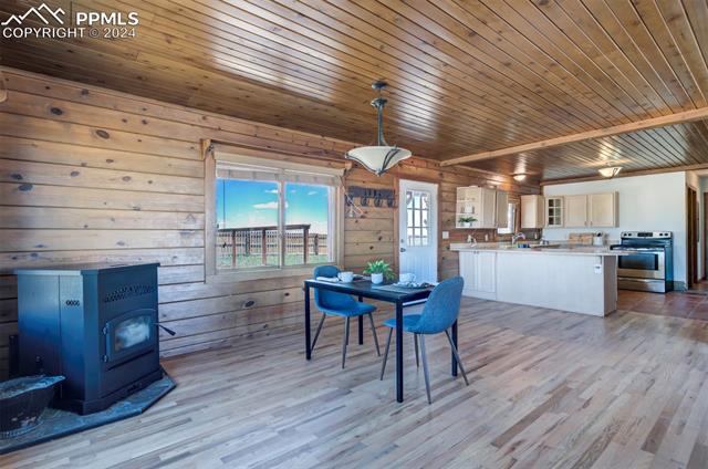 19350 Lemesany Road Calhan, CO 80808 - Photo 15 of 46 Dining space featuring wood walls, wooden ceiling, light hardwood / wood-style flooring, and a pellet stove