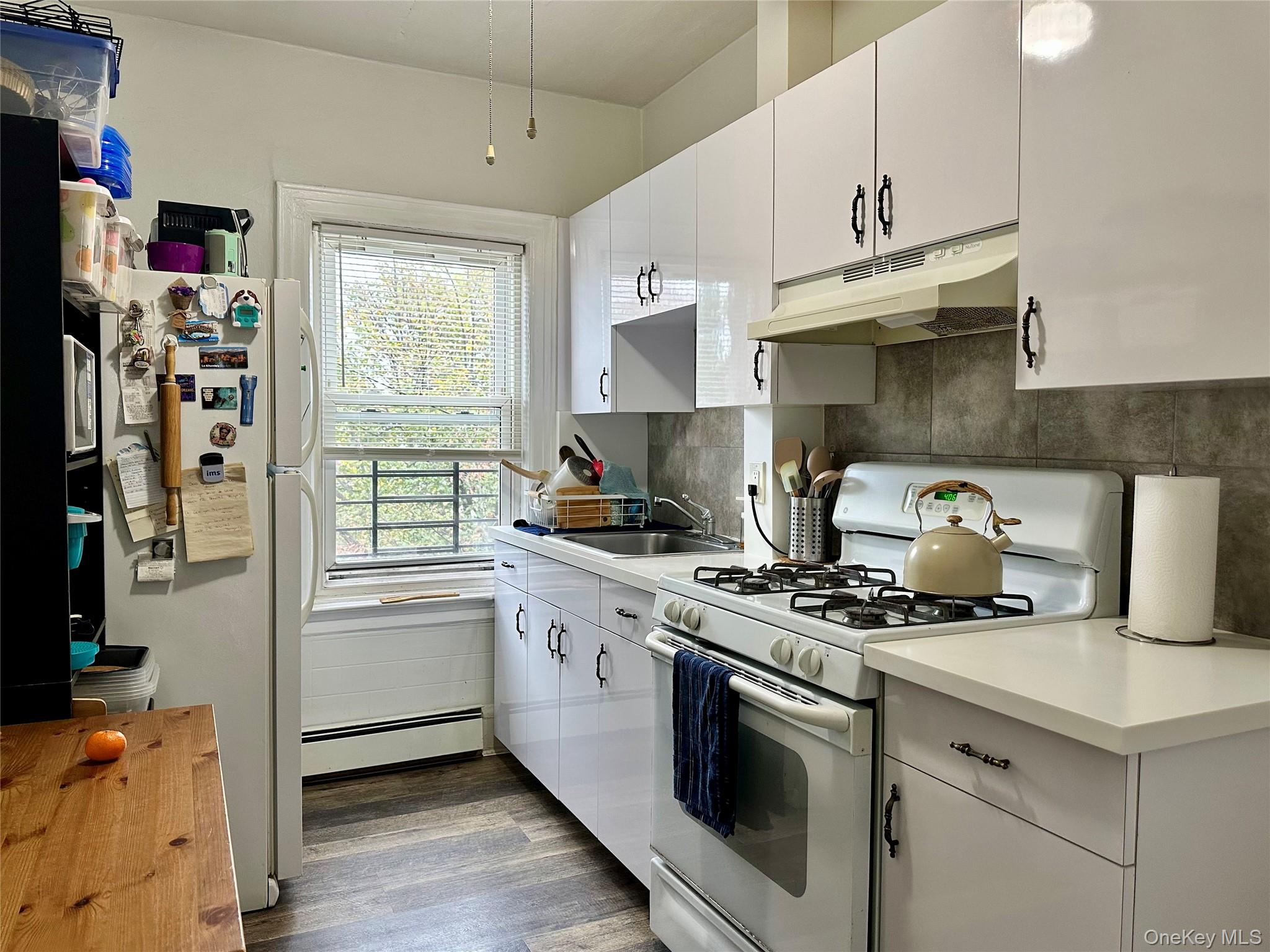 96-06 134th Road Queens, NY 11417 - Photo 6 of 11 Kitchen featuring white appliances, white cabinetry, light countertops, under cabinet range hood, and dark wood finished floors