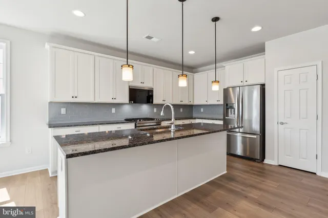 a kitchen with stainless steel appliances granite countertop a sink a stove a refrigerator and island with wooden floor