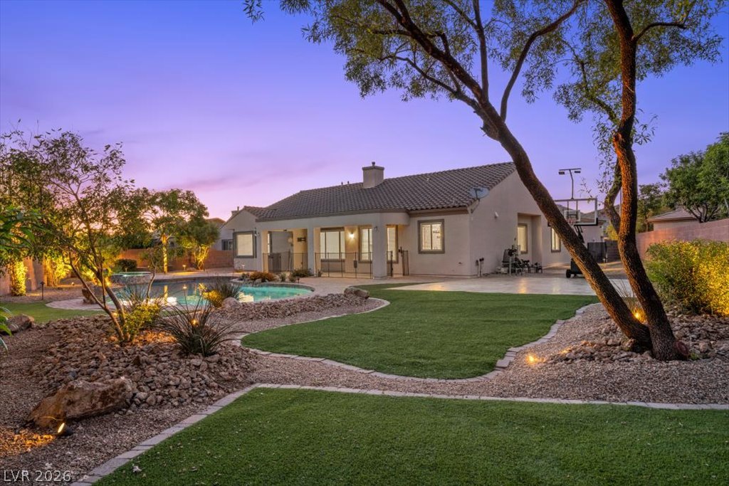 2125 De Rouge Avenue Henderson, NV 89044 - Photo 20 of 96 An inviting backyard features a sparkling pool and a lush, green lawn under a twilight sky.