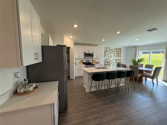 a kitchen with stainless steel appliances kitchen island granite countertop a refrigerator a stove a sink a dining table and chairs with wooden floor