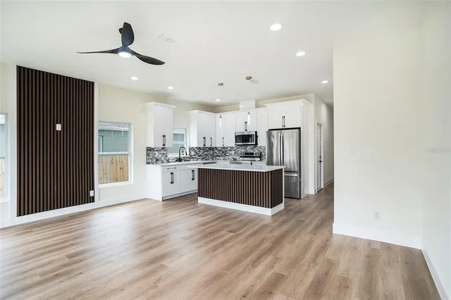 a large kitchen with stainless steel appliances a large counter top a refrigerator and cabinets