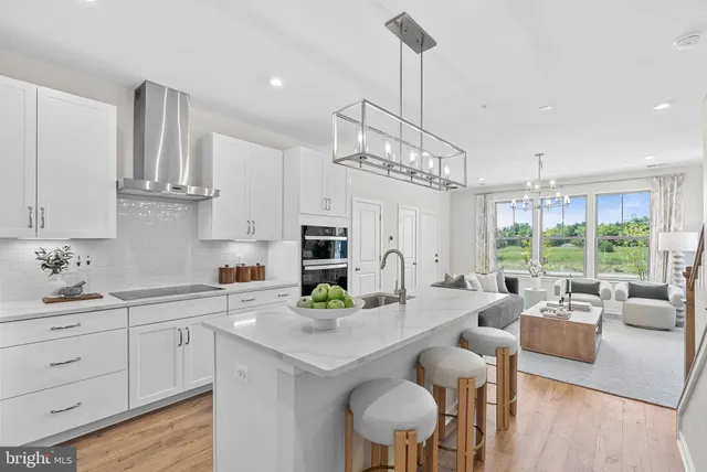 a kitchen with stainless steel appliances a sink a stove a refrigerator a dining table and chairs with wooden floor