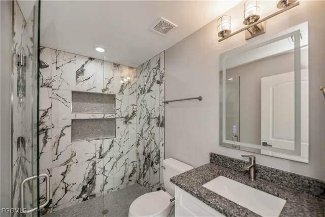 a bathroom with a granite countertop sink a toilet and shower