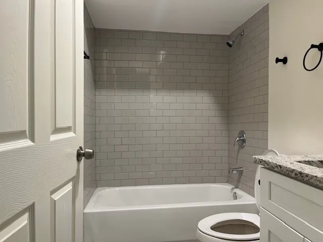 a bathroom with a granite countertop bathtub shower sink vanity and toilet