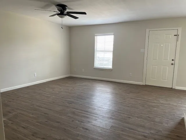an empty room with wooden floor a ceiling fan and windows