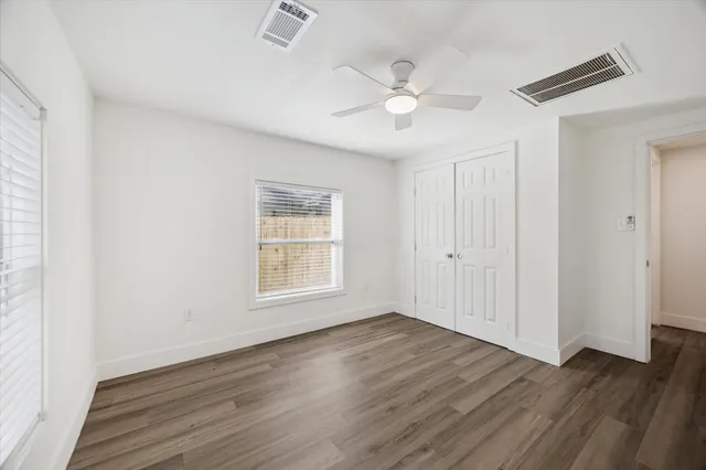 an empty room with wooden floor fan and windows