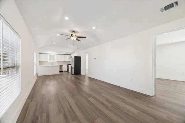 an empty room with wooden floor kitchen view and a window