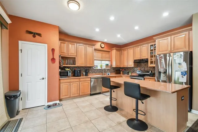 a kitchen with stainless steel appliances kitchen island granite countertop a refrigerator oven stove a sink a dining table and chairs with wooden floor