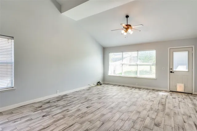 an empty room with wooden floor chandelier fan and windows