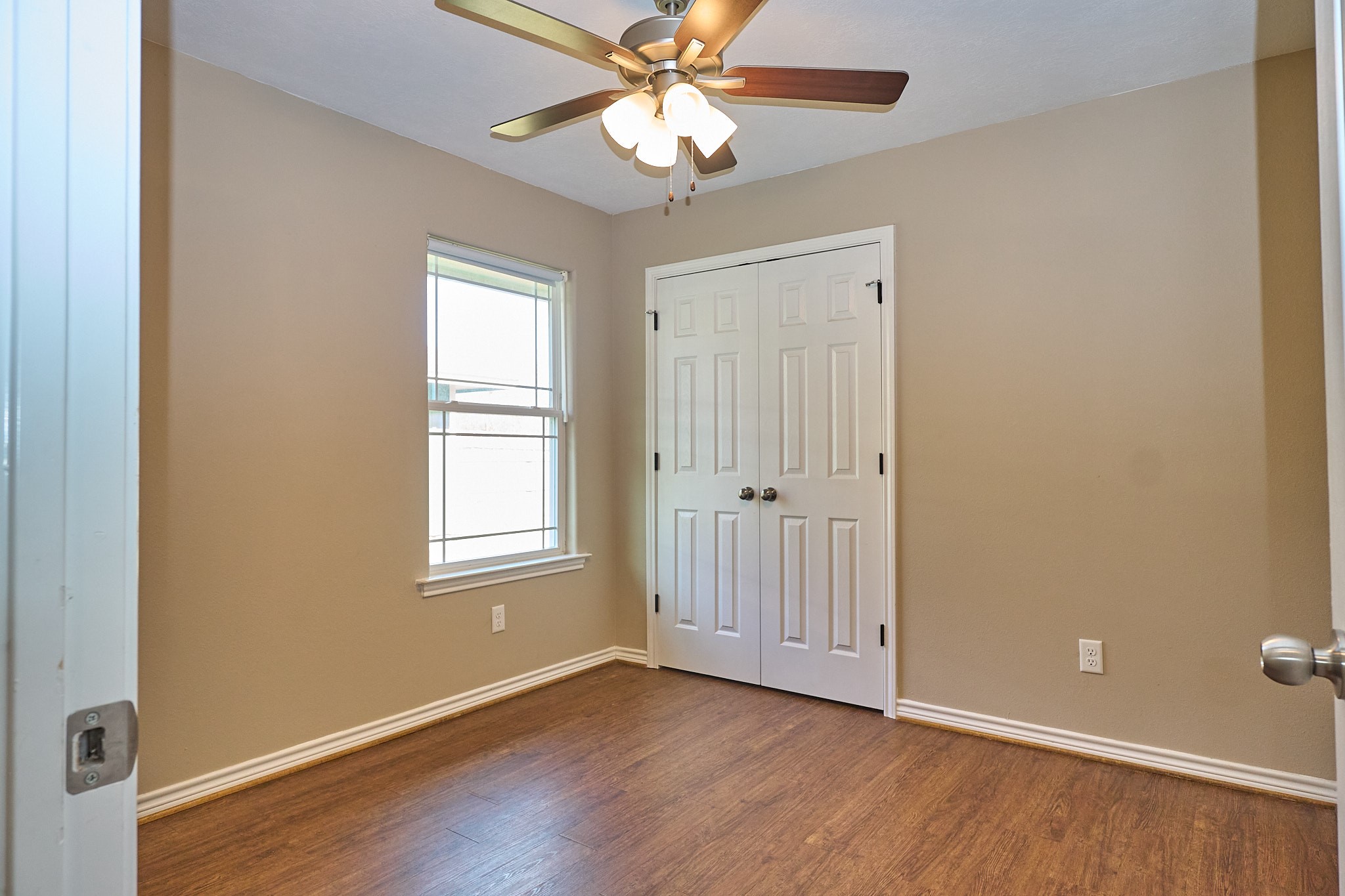 1807 Nuches Lane Bryan, TX 77803 - Photo 20 of 27 This room features neutral-colored walls, a ceiling fan with lights, a window for natural light, and a double-door closet. The hardwood floor adds warmth, making it a versatile space.