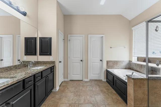 a spacious bathroom with a granite countertop double vanity sink a mirror and a bathtub