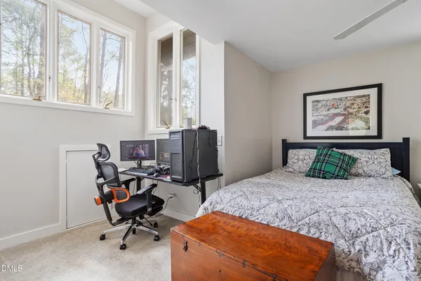 a bedroom with a bed a computer on the desk and a dresser next to a window