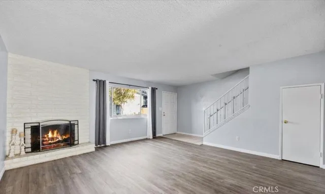 a view of an empty room with wooden floor fireplace and a window