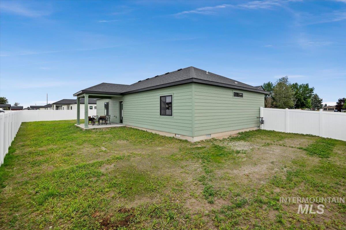 1201 Jade Drive Rupert, ID 83350 - Photo 26 of 27 Rear exterior featuring green horizontal siding, a covered patio, a dark shingle roof, black-framed windows, and a white vinyl fence enclosing a grass yard