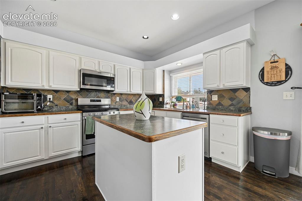 8347 Tibbs Road Peyton, CO 80831 - Photo 2 of 39 Kitchen featuring white cabinetry, stainless steel appliances, a central island, patterned tile backsplash, and wood-finish flooring