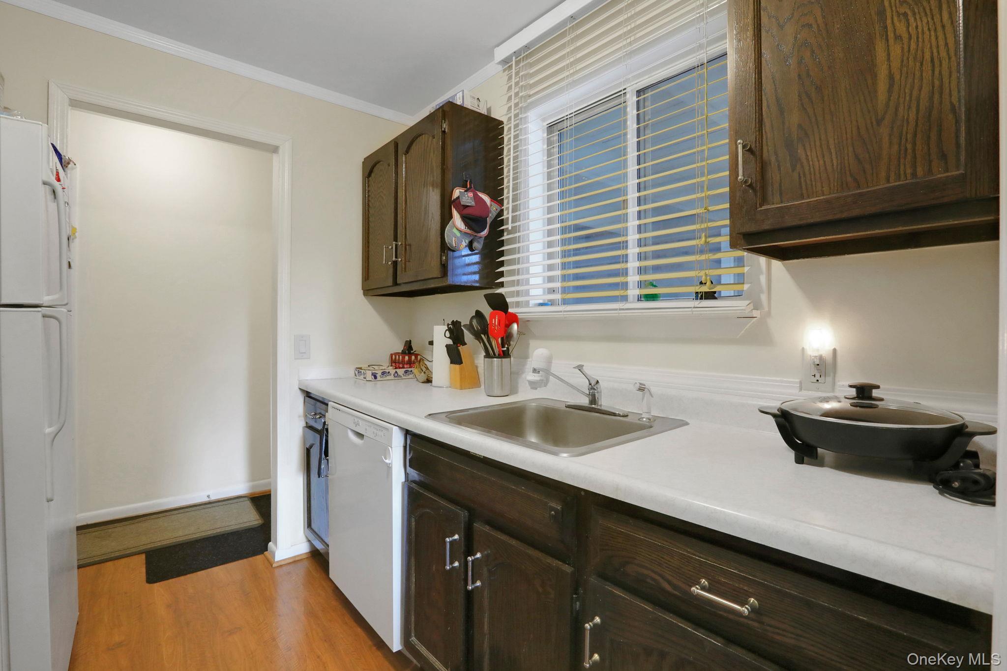 302 Commons Way, Unit E Fishkill, NY 12524 - Photo 16 of 26 Kitchen featuring light countertops, white appliances, light wood-type flooring, dark brown cabinetry, and crown molding