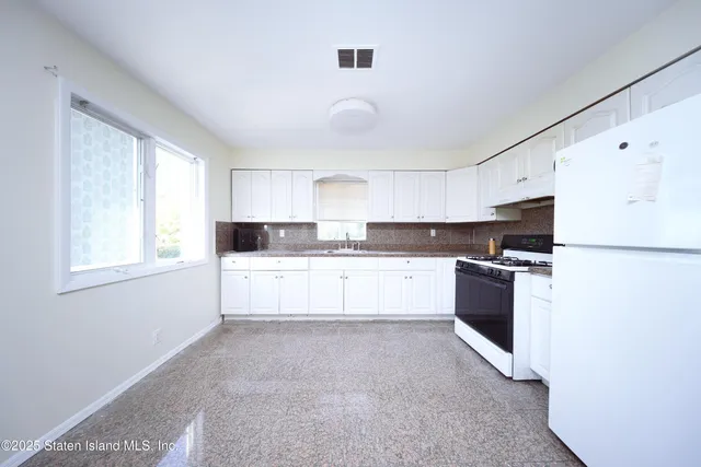 a large white kitchen with granite countertop a stove top oven a sink dishwasher and a refrigerator with wooden floor