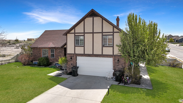 View of front of house featuring a front yard, brick siding, an attached garage, and stucco siding