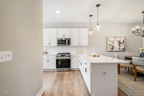 a kitchen with stainless steel appliances a stove top oven a sink a refrigerator a dining table and chairs with wooden floor