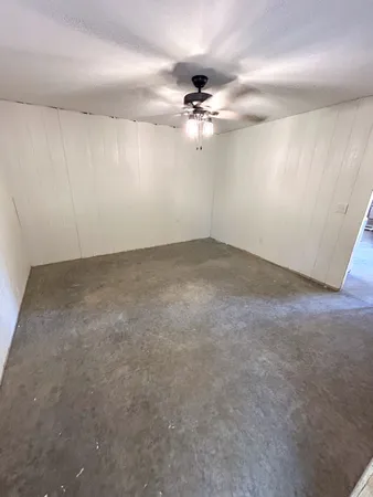 an empty room with a chandelier fan and windows