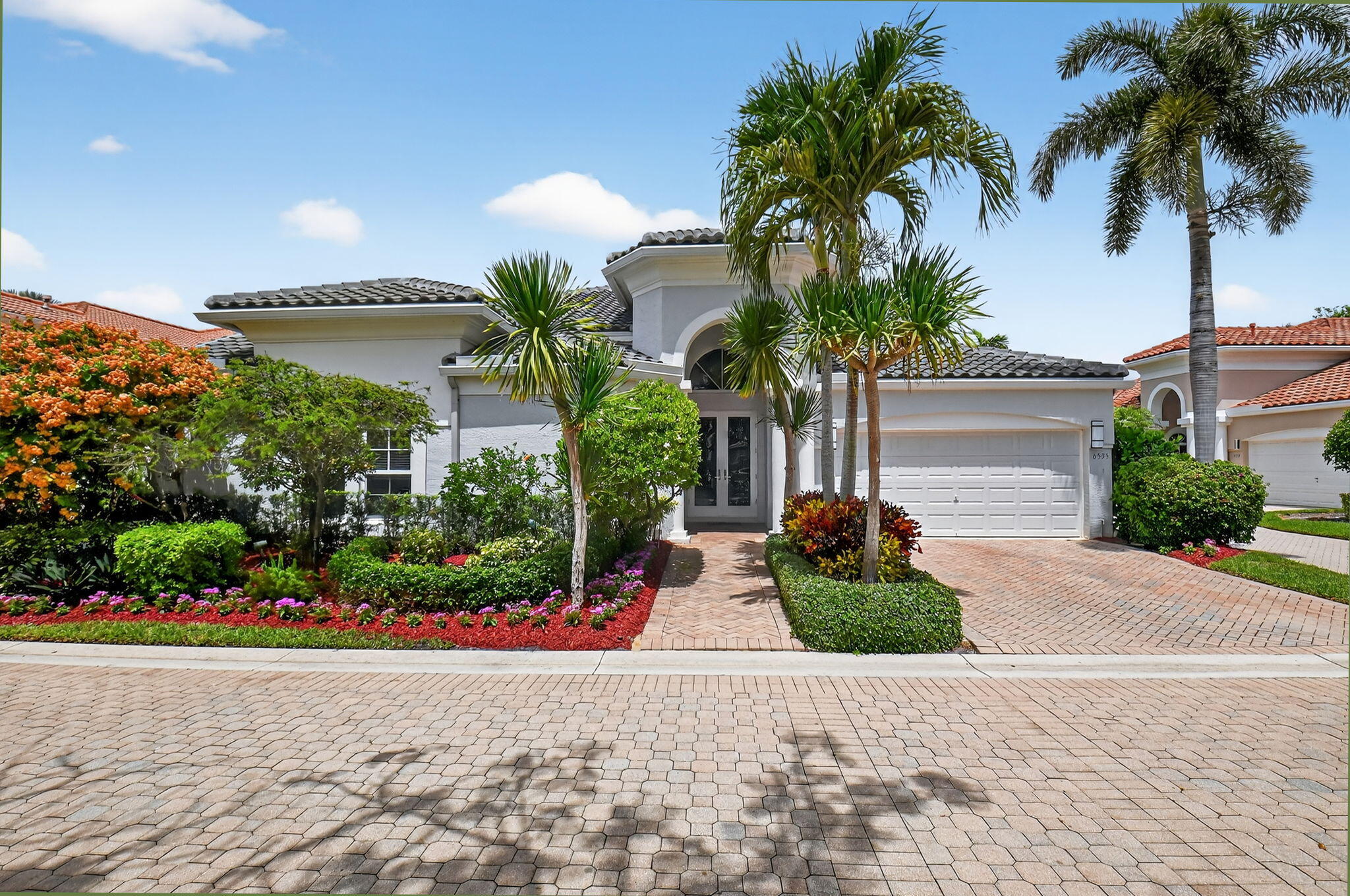 a palm tree sitting in front of a house with a garden