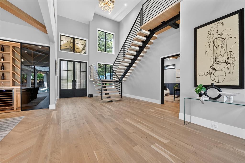 11028 Edgemere Road Dallas, TX 75230 - Photo 10 of 40 Two-story foyer featuring light wood-finish flooring, a modern floating staircase with metal railings, and a built-in beverage bar with a wine cooler