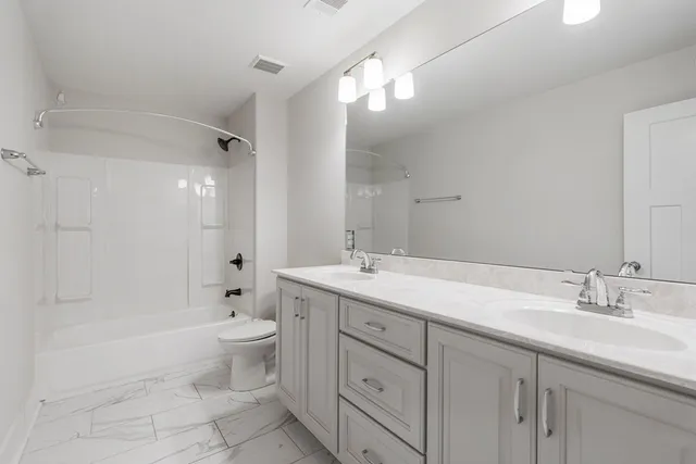 a spacious bathroom with a double vanity sink toilet mirror and bathtub