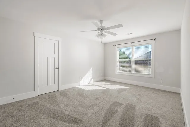 an empty room with chandelier fan and windows