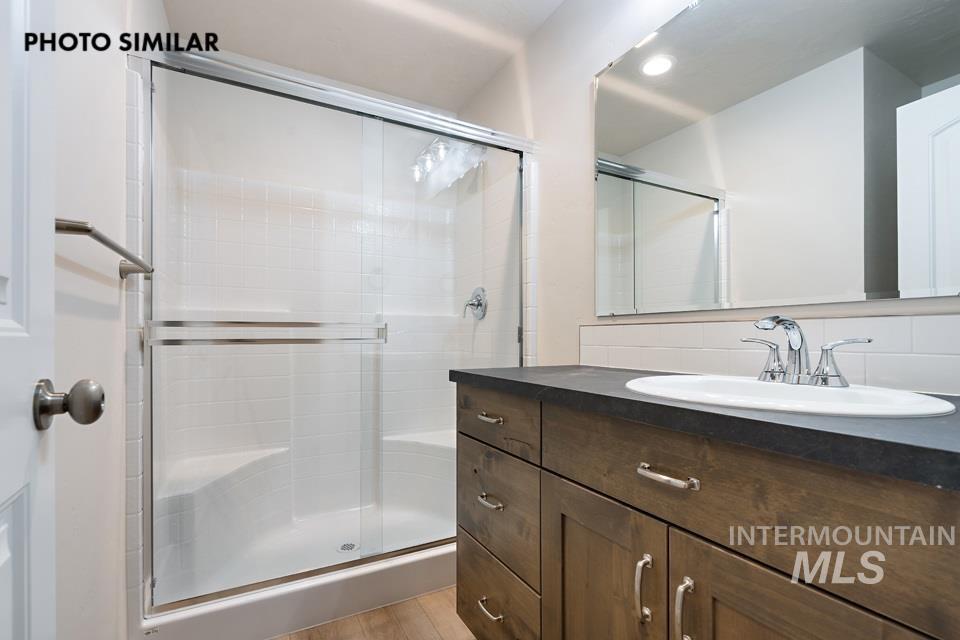 1645 Haystack Emmett, ID 83617 - Photo 29 of 33 Shower with glass enclosure and integrated bench seating, alongside a vanity featuring wood-finish cabinetry, a dark countertop, an undermount sink, and a framed mirror