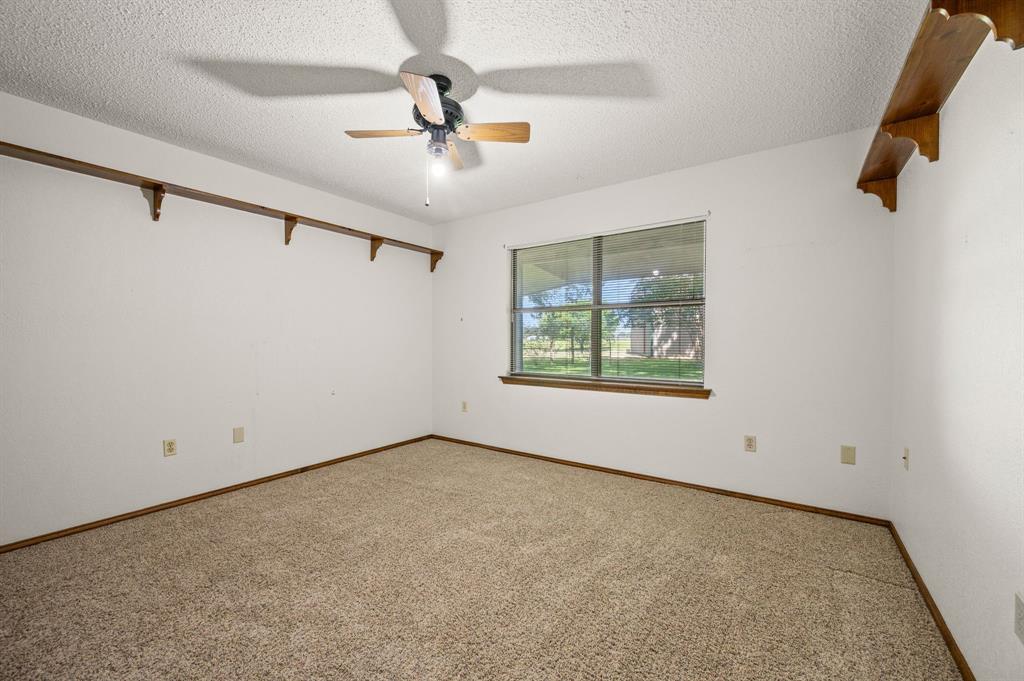 515 New Highland Road Springtown, TX 76082 - Photo 22 of 38 Carpeted room featuring a ceiling fan with integrated lighting, a window with exterior visibility, wood trim, and wall-mounted shelving