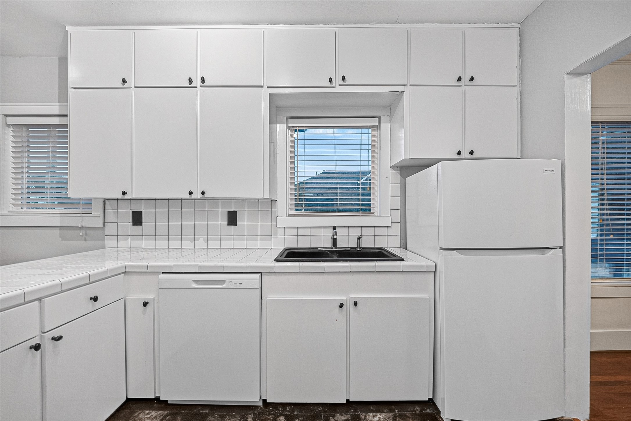 1758 Hawthorne Street, Unit 2 Houston, TX 77098 - Photo 10 of 19 This kitchen features modern black granite countertops, sleek white cabinetry with glass fronts, and a stylish black and gray tile backsplash. It is equipped with essential appliances and has a track lighting system, offering a functional and contemporary space. The neutral gray walls complement the overall design, leading into a room with hardwood flooring.