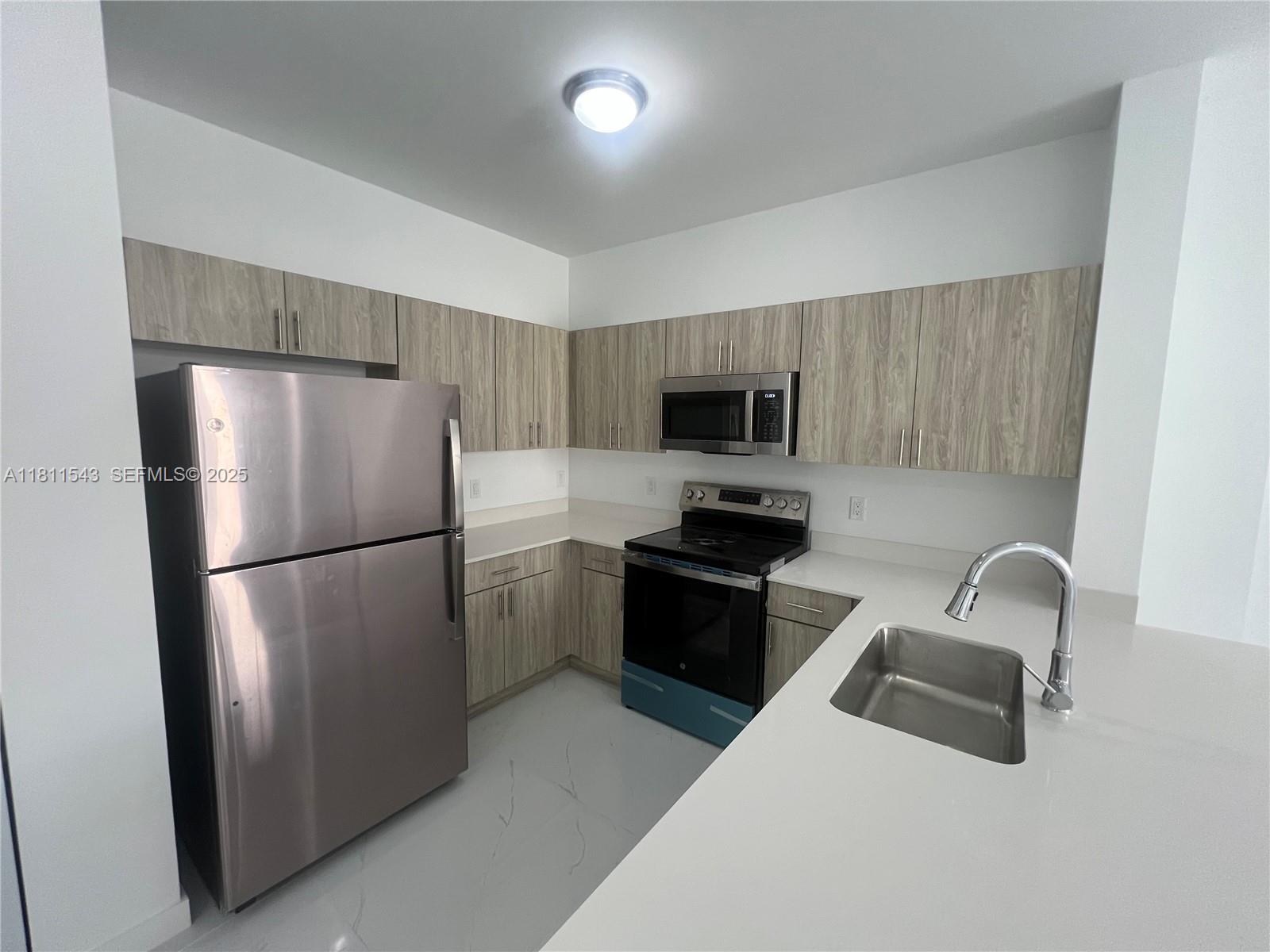 1010 Southwest 69th Avenue, Unit 104 Miami, FL 33144 - Photo 8 of 16 a kitchen with a refrigerator a microwave a stove and cabinets