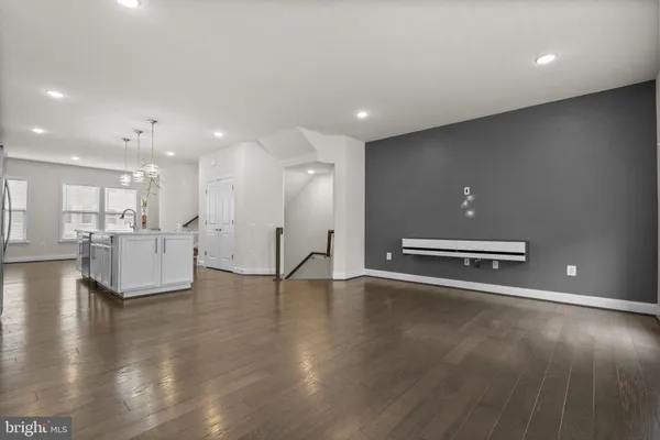 a view of an empty room with wooden floor and a kitchen