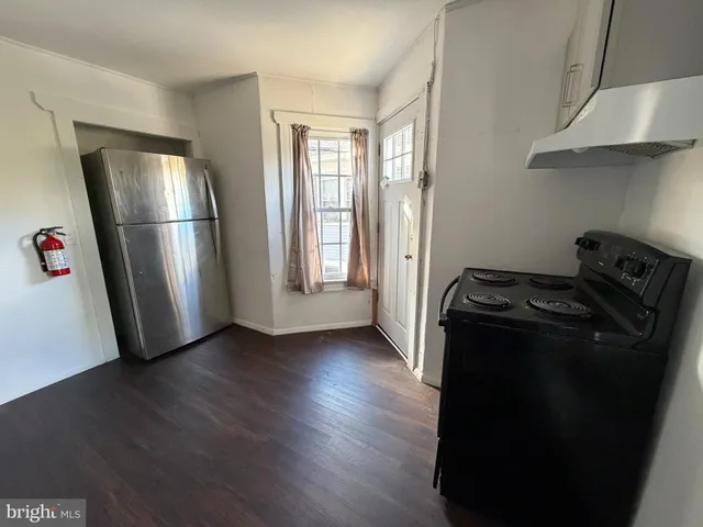 a view of a refrigerator in kitchen and an empty room with wooden floor